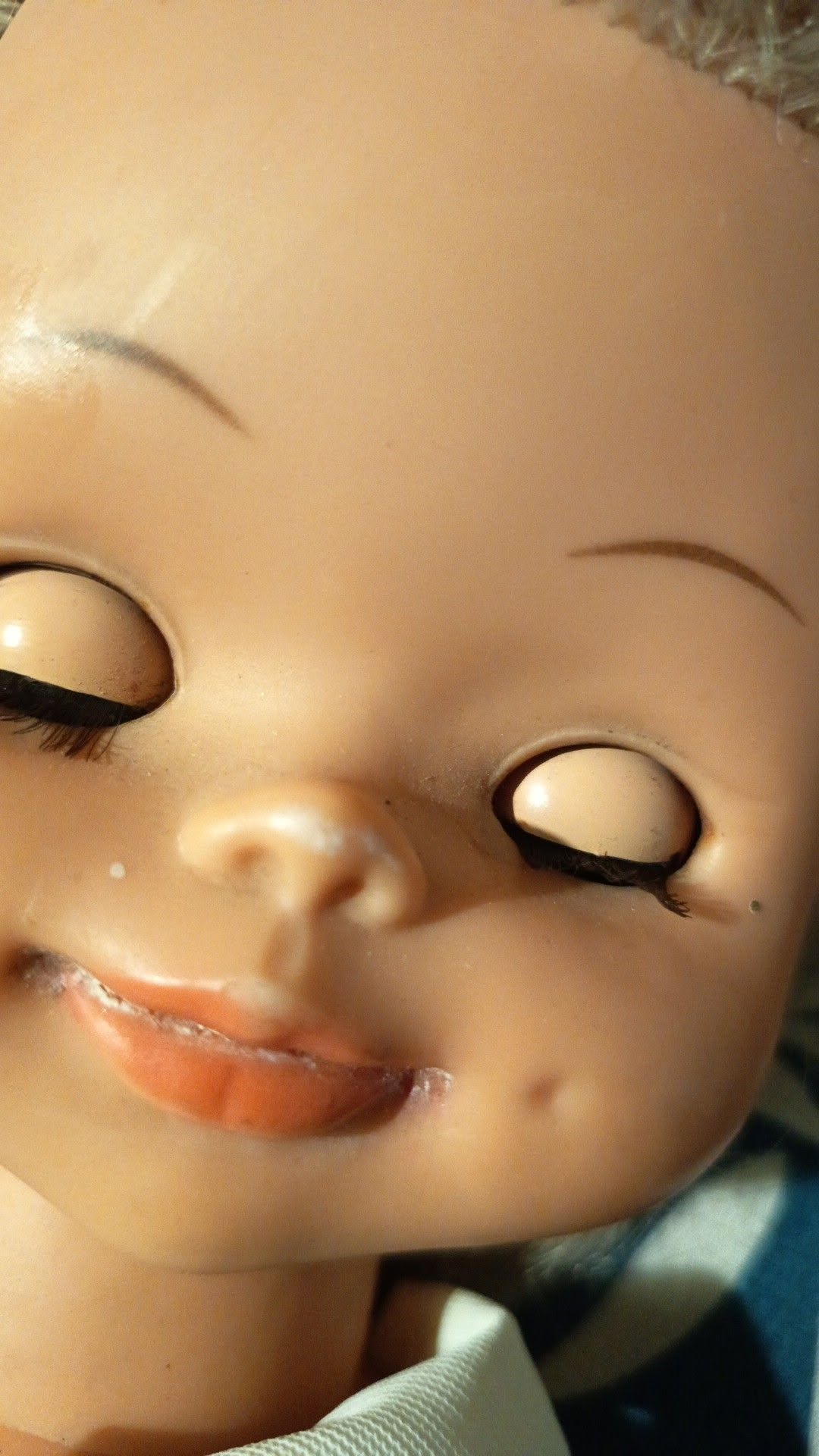 « Delphine », poupée Bella — collection de Sylvie — Gros plan du visage de Delphine, la Bella de Sylvie : yeux fermés bordés de cils sombres, sourcils fins, sourire et petites fossettes. Les traces du temps autour des lèvres sont conservées — vue 2.