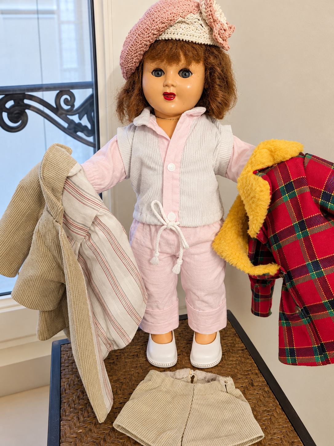 Poupée Gégé — les tenues de Mireille — La poupée en tenue pastel, présentée avec plusieurs vêtements, dont un manteau écossais — vue 1.