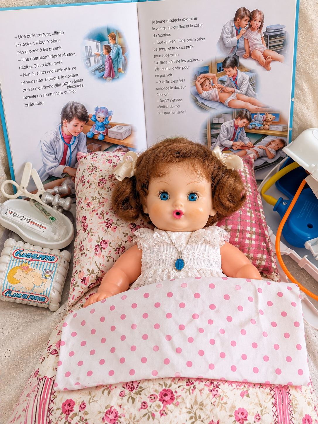 Bébé mouilleur et soigneur Bella, 32 cm — souvenir d’enfance de Mireille — Bébé Bella de Mireille présenté au lit avec ses accessoires de jeu — vue 1.